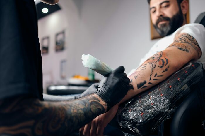 A tattoo artist applying a new tattoo on a client's arm, highlighting the risks of permanent spelling errors.