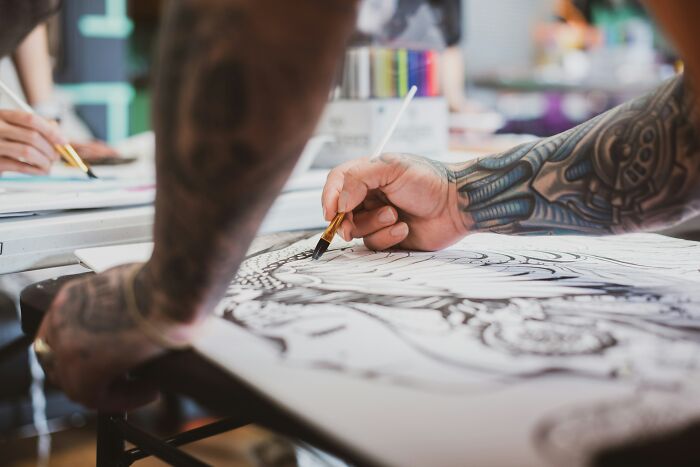 A heavily tattooed artist meticulously drawing a design, illustrating the artistic process before making a permanent tattoo.