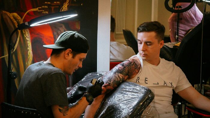 A client observing as a tattoo artist works on a large arm tattoo, illustrating the client-artist interaction.