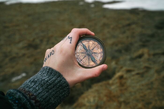 A hand holding a compass with a small tattoo on the fingers, symbolizing the permanence of tattoos and possible errors.