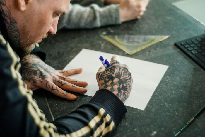 A person with tattooed hands drawing a design, emphasizing the creative process of tattoo artists.