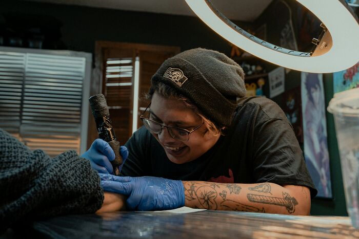 A happy tattoo artist creating a permanent tattoo on a client's arm, displaying the joy of tattoo artists at work.