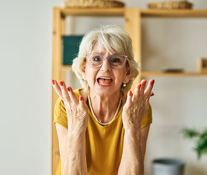 A senior woman with glasses and red nail polish looks frustrated, with hands raised, relating to the lung donation conflict. A senior woman with glasses and red nail polish looks frustrated, with hands raised, relating to the lung donation conflict.