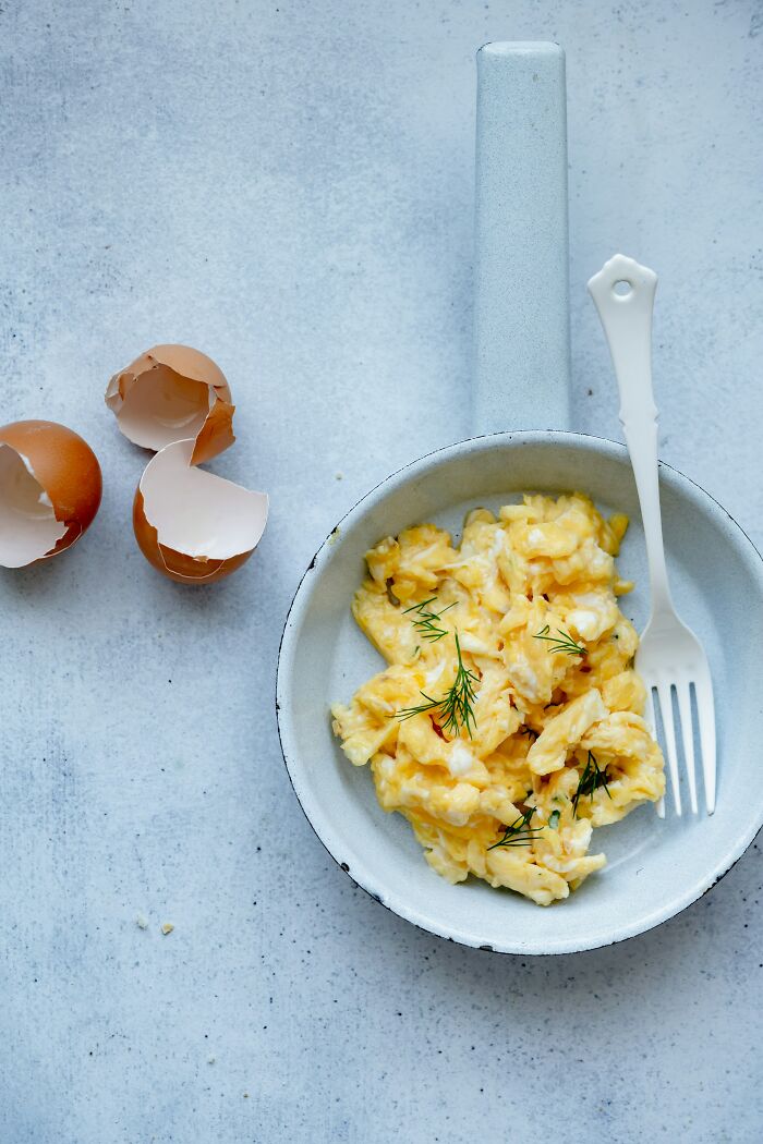 Scrambled eggs in a pan with eggshells beside it, a secret companies might not want you to know about food prep.