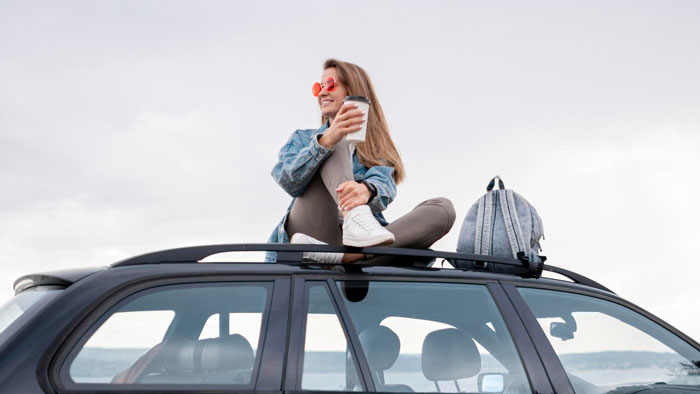 Woman sitting on a car roof, enjoying coffee, representing one of the 5 things a mortician advises.