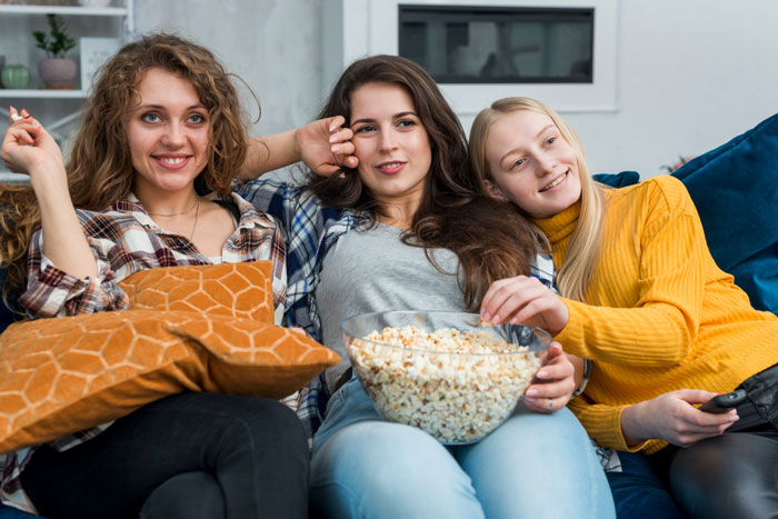 Three young women, a picky eater, enjoy a movie night on a couch with a bowl of popcorn. Three young women, a picky eater, enjoy a movie night on a couch with a bowl of popcorn.