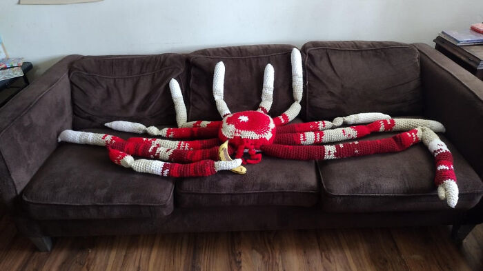 A large red and white crochet spider creation laid out on a brown couch.