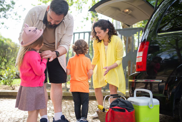 A family with two young children loading a car for a family vacation, a woman takes nanny on family vacation.