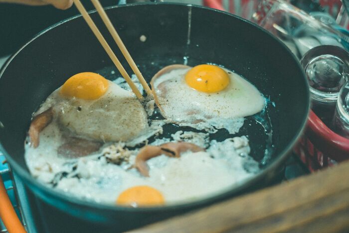 Eggs and ham frying in a black pan, with chopsticks turning them, illustrating interesting facts about cooking breakfast.