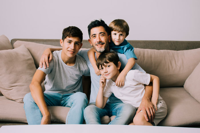 A happy dad with his three sons on a couch, illustrating a family not separated by blood or adoption. A happy dad with his three sons on a couch, illustrating a family not separated by blood or adoption.