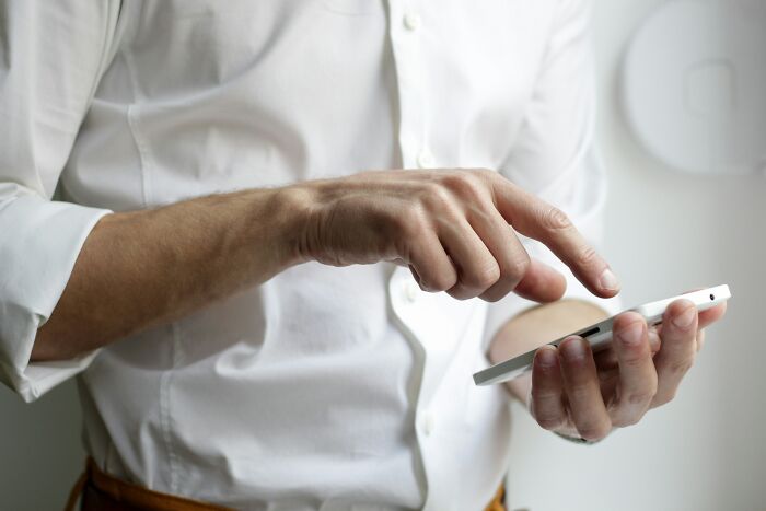 A person in a white shirt subtly scrolls on a smartphone, displaying signs someone isn't as nice as they pretend to be.