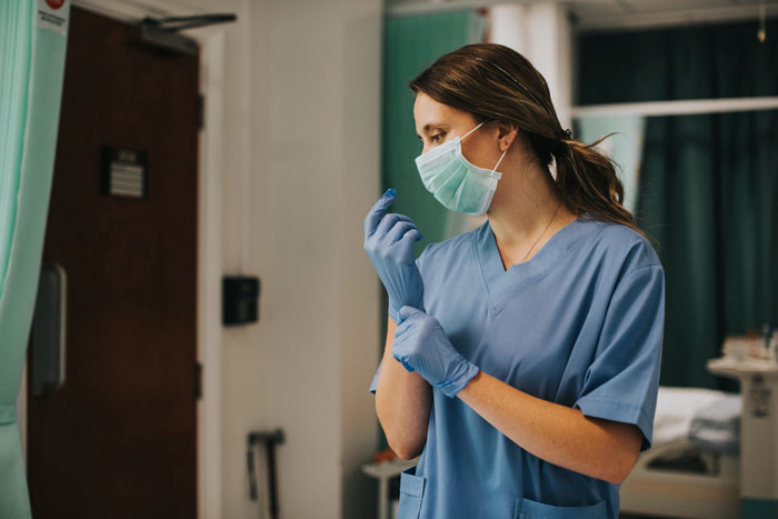 A woman in nurse scrubs and mask, wearing gloves, embodying a mom in nurse mode during DIL's delivery.