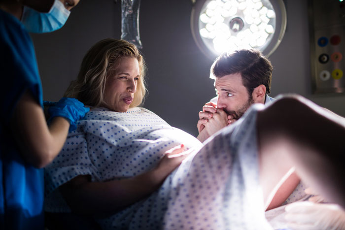 A nurse tends to DIL during delivery, as husband holds her hand, during a family moment with mom.