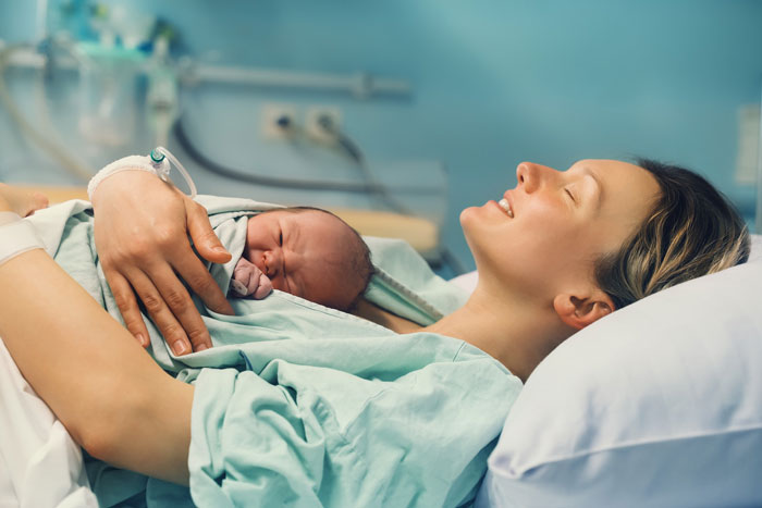 A new mother smiles, holding her newborn close after delivery, embodying the joyful nurse mode.
