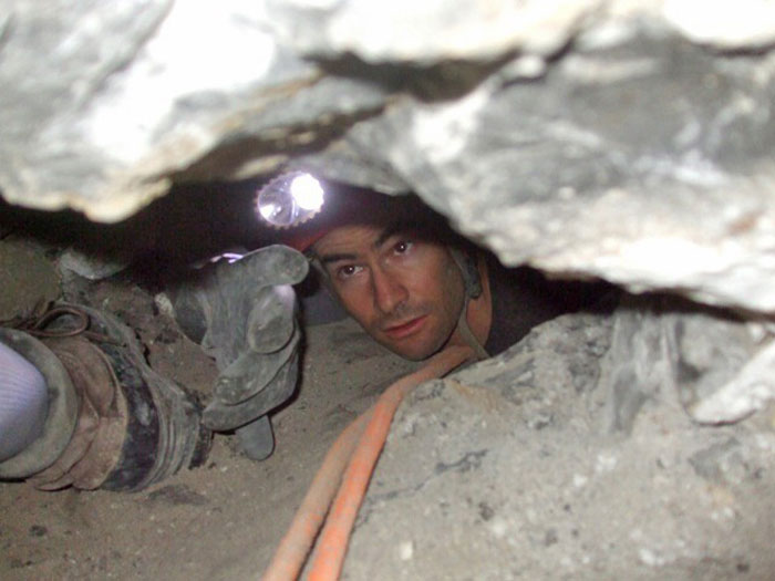 A cave rescuer bravely navigates the narrow passage of Nutty Putty Cave, headfirst, to reach the trapped man.