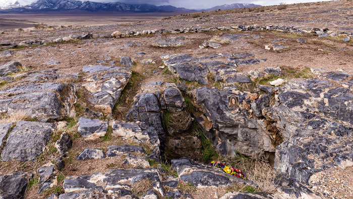 The rocky, open-air entrance to Nutty Putty Cave, with mountains in the background and a memorial for the trapped man.