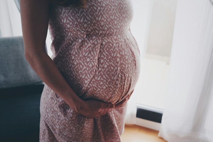 A pregnant woman in a patterned dress gently cradling her belly, reflecting topics beyond mansplaining.