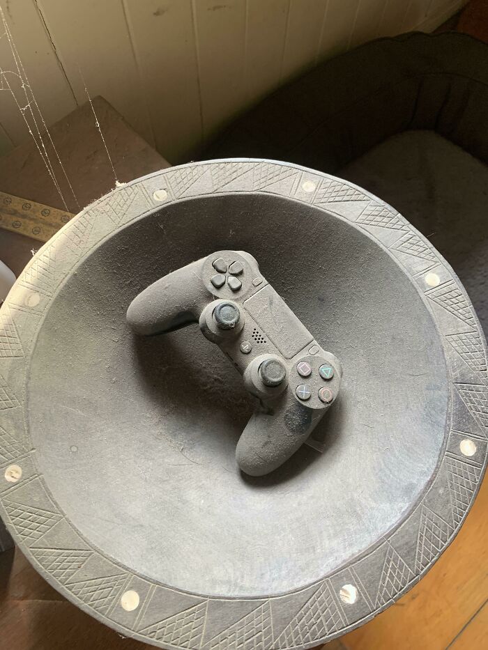 A PlayStation controller covered in a thick layer of dust, an incredibly satisfying paint match due to its integration with the surface.