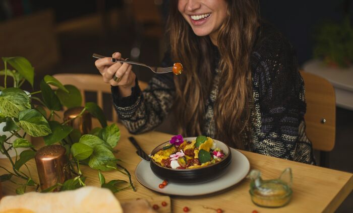 A woman with long brown hair smiles while eating a meal with international partners, experiencing culture shocks.