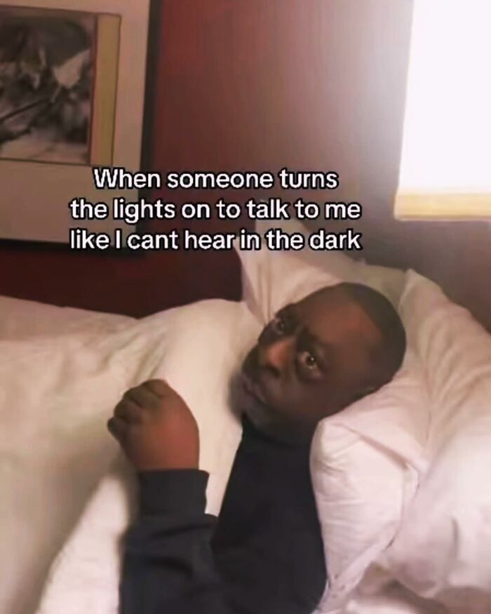 A relatable meme featuring a man in bed with the text 'When someone turns the lights on to talk to me like I cant hear in the dark.'