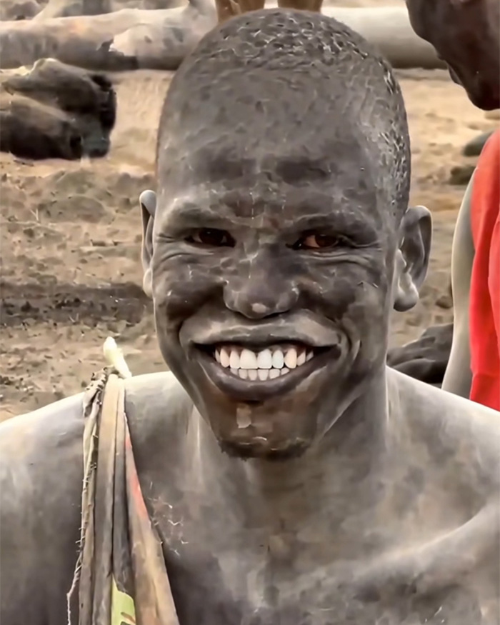 A man with a mud-covered face displays a wide white smile after using an African twig for dental hygiene. A man with a mud-covered face displays a wide white smile after using an African twig for dental hygiene.