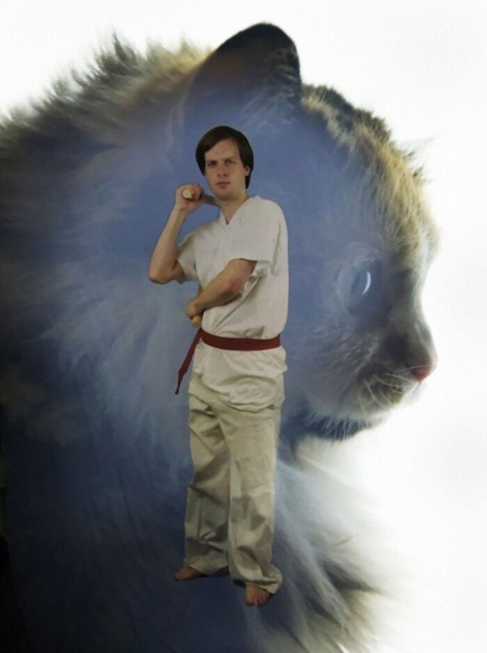 A man in a martial arts uniform holding nunchucks, with a translucent cat overlay behind him, a ridiculous animal photo.