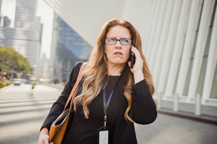 A woman with long hair and glasses looks concerned while on a phone call, stories about MILs.