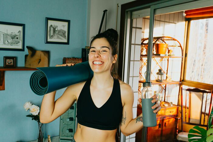 A smiling woman holding a yoga mat and water bottle, representing MILs stories and a vengeful spirit.