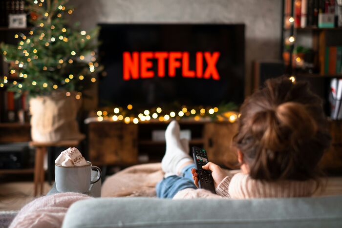 A person relaxing on a couch, watching Netflix on a large TV, illustrating MILs stories and a vengeful spirit.