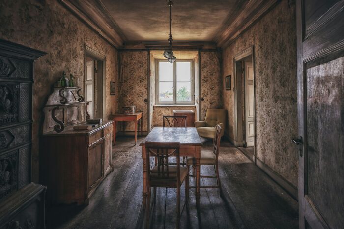 An old, dimly lit room with distressed wallpaper, antique furniture, and a window, representing MILs stories.