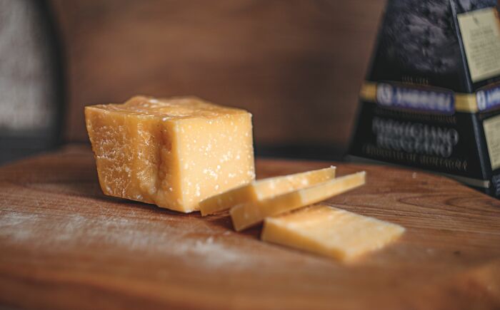 A block of Parmesan cheese with several slices on a wooden cutting board, representing MILs stories.