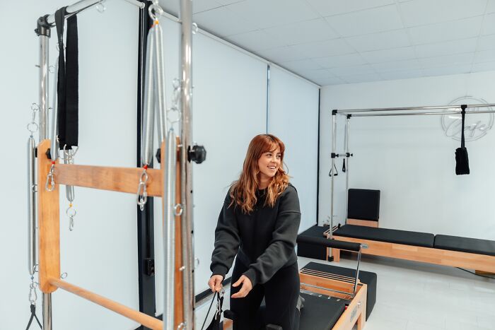 A woman smiling while exercising with a Pilates reformer, stories about MILs.