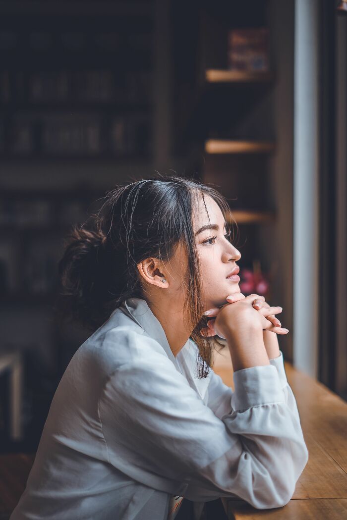 A young woman with her hair pulled back gazes out a window, contemplating life's unexpected twists and turns.