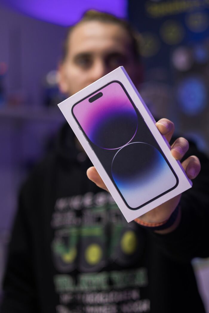 A person holding up a new smartphone in a box, hinting at behind the scenes secrets companies don't want you to know.