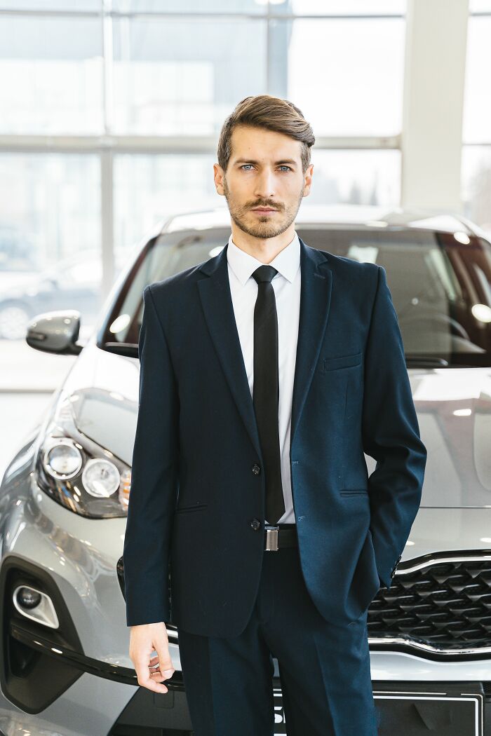 A man in a suit stands in front of a car, depicting a final day at work story.