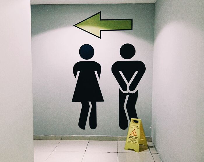 A restroom sign with male and female figures and a green arrow pointing left. Fascinating things about the world.