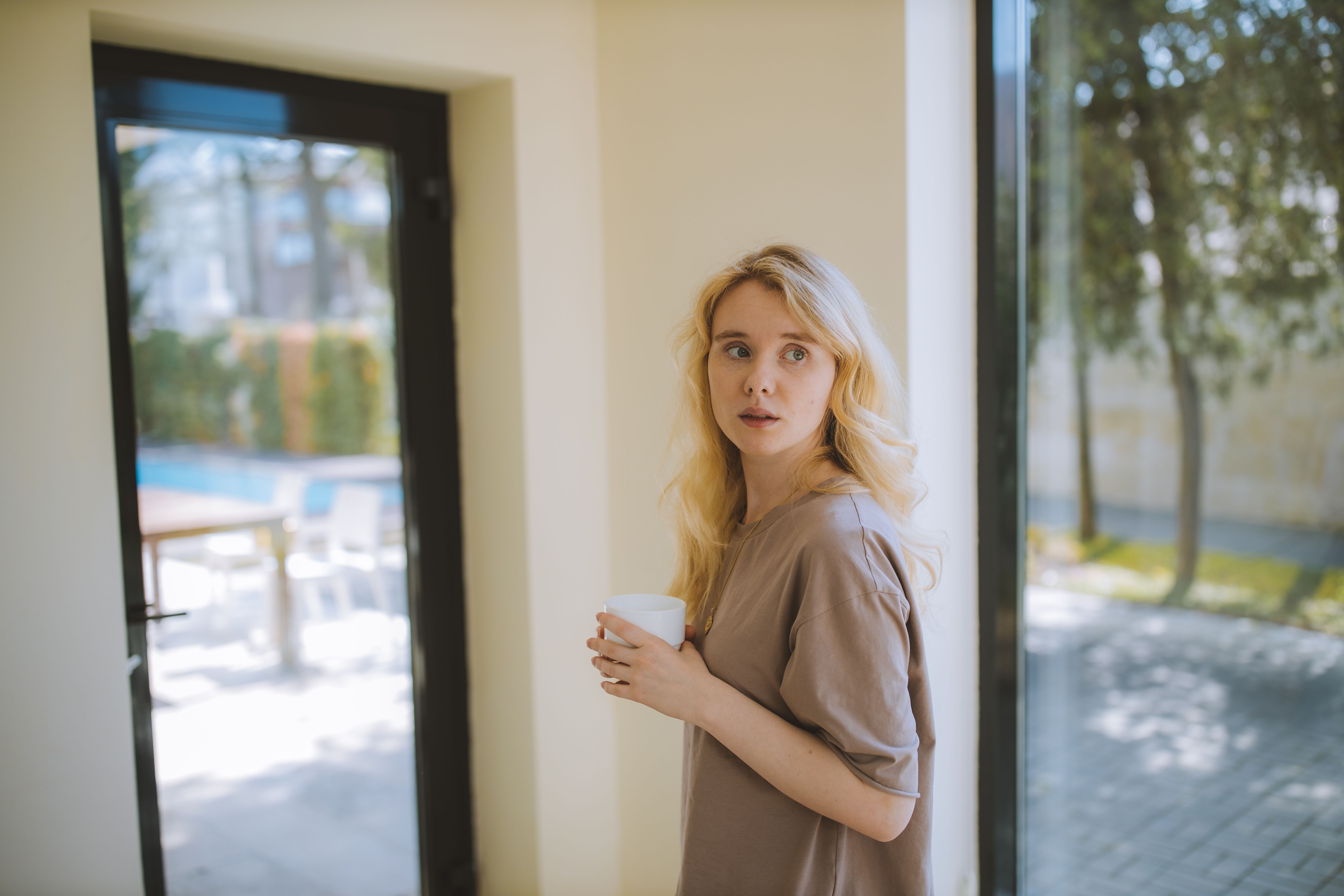 A blonde woman with a scared expression, holding a white mug, representing a woman's scary fixation over a groom.