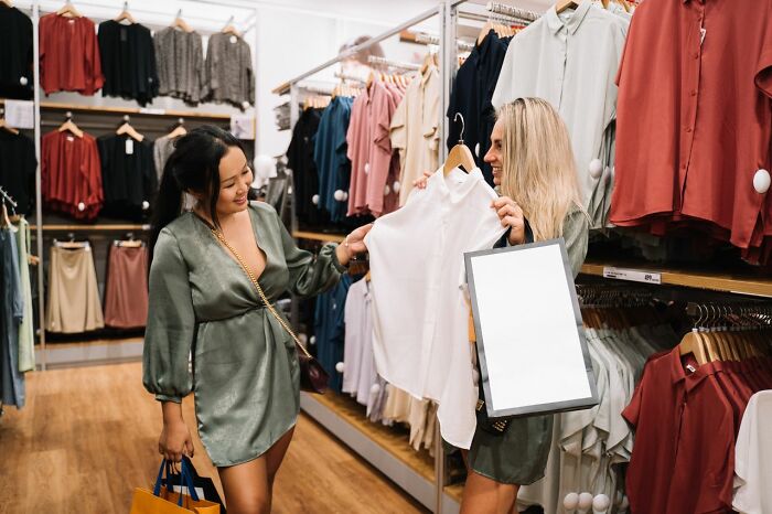 Two women shopping, one holding a white shirt, sharing behind the scenes secrets companies don't want you to know.