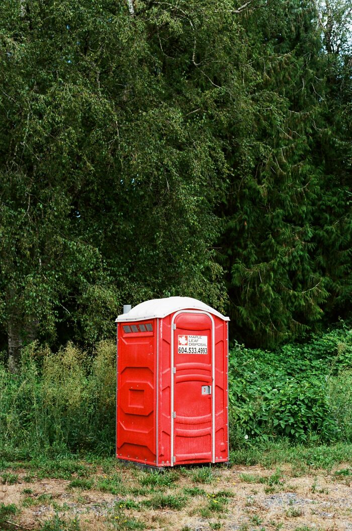 A red portable toilet in a grassy area with trees, symbolizing the shocking and unusual ways people have lost their lives.