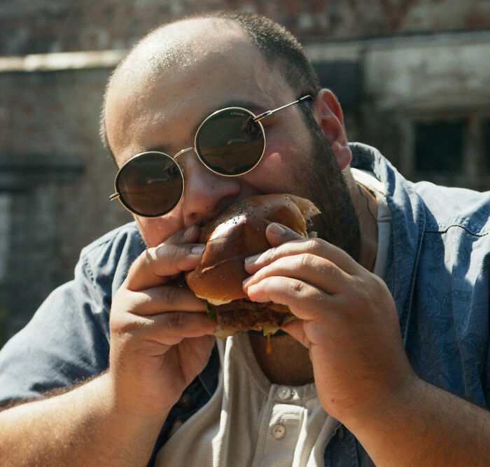 A man wearing sunglasses taking a large bite out of a burger, representing the consumption of trendy snack food.