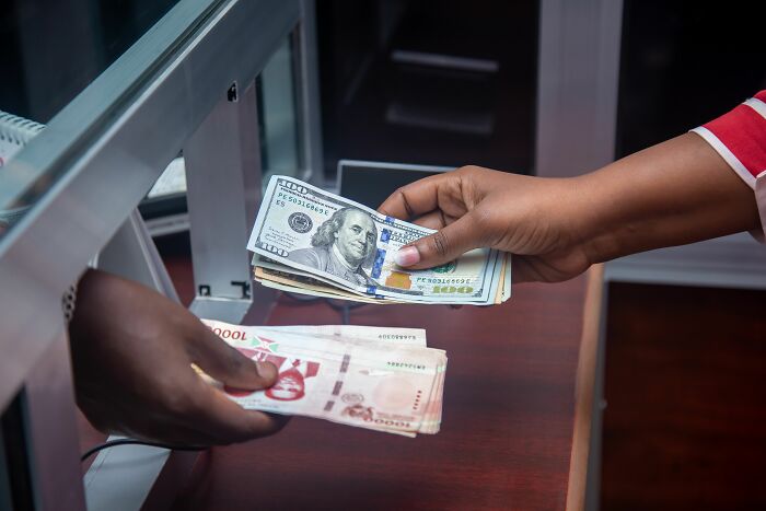 Hands exchanging US dollar bills and local currency at a bank. One of the dumbest reasons people got fired.