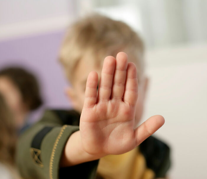 A blurred child holding up a hand to signal stop, representing a reaction to mistreating classmate with cancer. A blurred child holding up a hand to signal stop, representing a reaction to mistreating classmate with cancer.