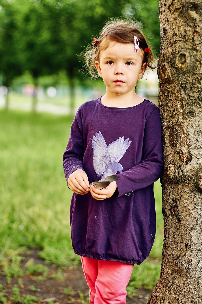 A young girl stands by a tree in a park, holding a leaf, symbolizing unexpected twists and turns in life.