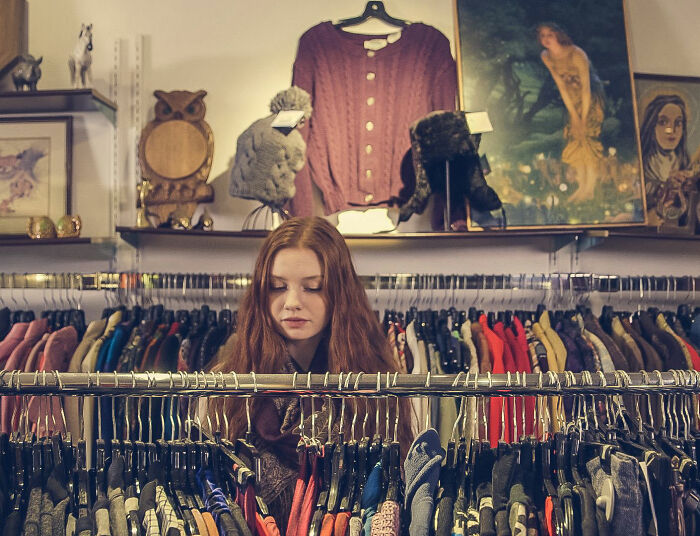 A young woman with long red hair looking through a rack of clothes. This image relates to clothing sizes and dress experiments. A young woman with long red hair looking through a rack of clothes. This image relates to clothing sizes and dress experiments.