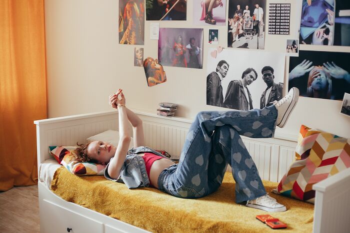 Millennial in 2000s pop culture themed room, lying on bed, surrounded by music posters and vintage items. Millennial in 2000s pop culture themed room, lying on bed, surrounded by music posters and vintage items.