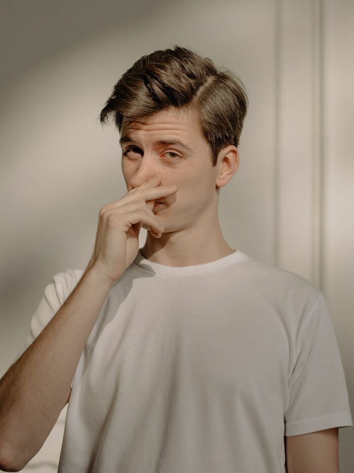 A man in a white t-shirt pinching his nose, showing one of the ridiculous HR problems.