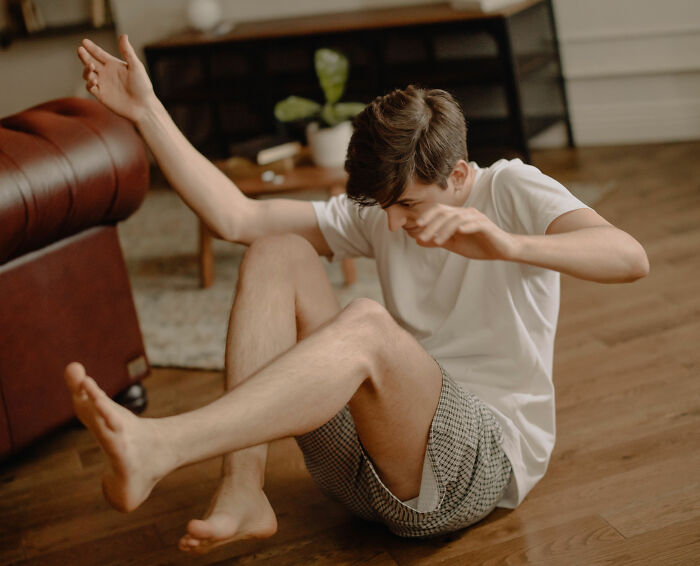 A young boy sitting on the floor, stretching his arms and legs, exploring his friend's house and their normal.
