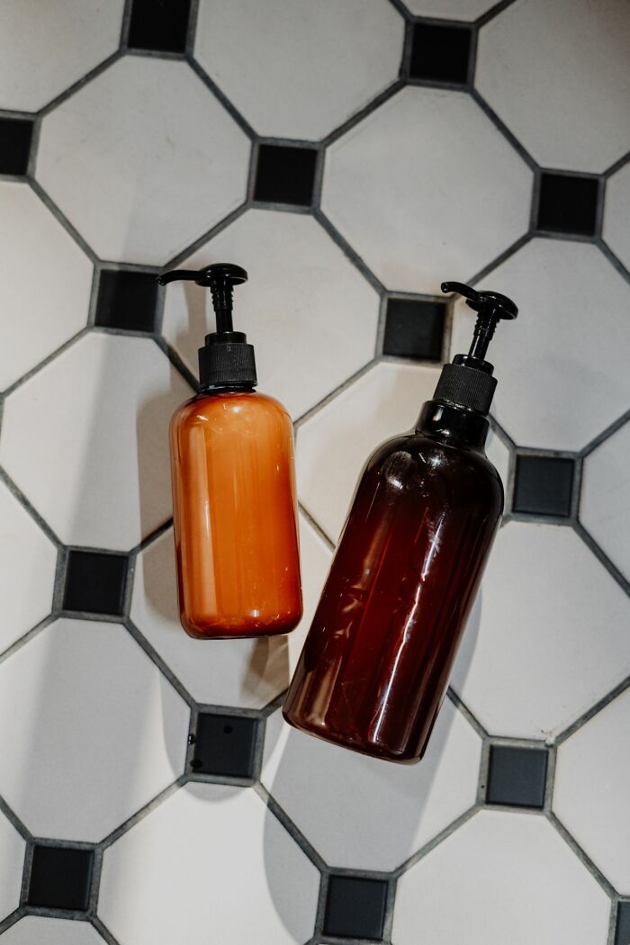 Two shampoo bottles lying on a black and white tiled floor.