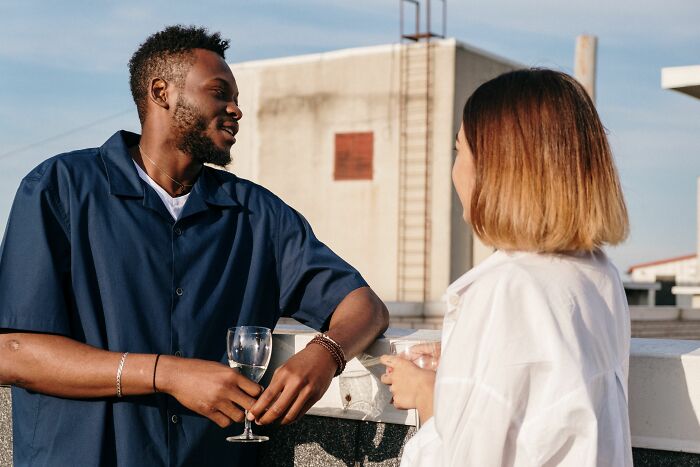 A man and woman talk on a rooftop with drinks, possibly about women changing their minds about perfect guys.