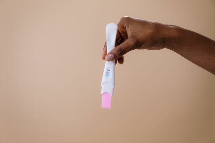 A hand holds a white pregnancy test with a positive result. This image relates to secrets and how they could do damage.